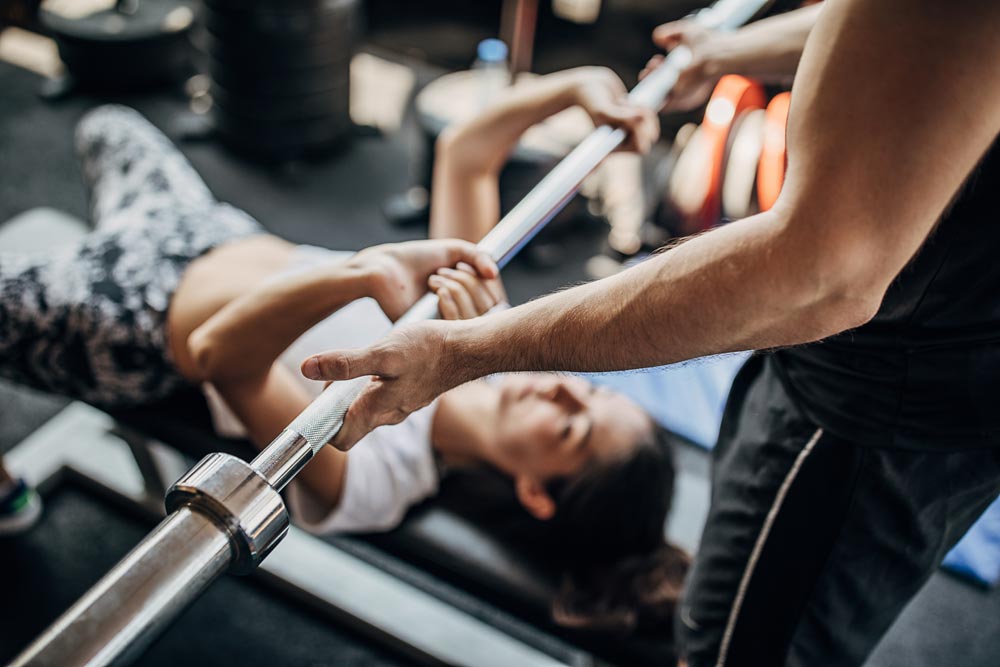 Woman exercising with a barbell with personal trainer