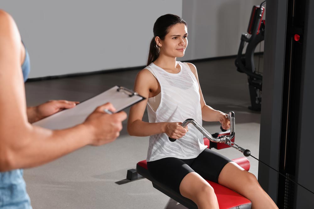 Woman doing exercise in gym while trainer is looking at workout plan