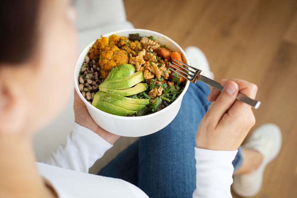 Woman eating fresh salad, avocado, beans and vegetables
